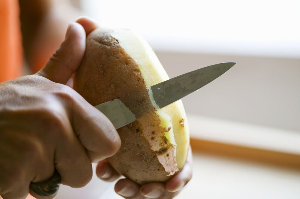 Eine Kartoffel wird mit einem Messer geschält