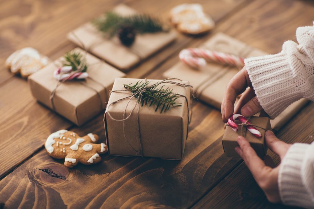 Frau, die Weihnachtsgeschenke auf Holzuntergrund mit nachhaltigen Materialien verpackt.