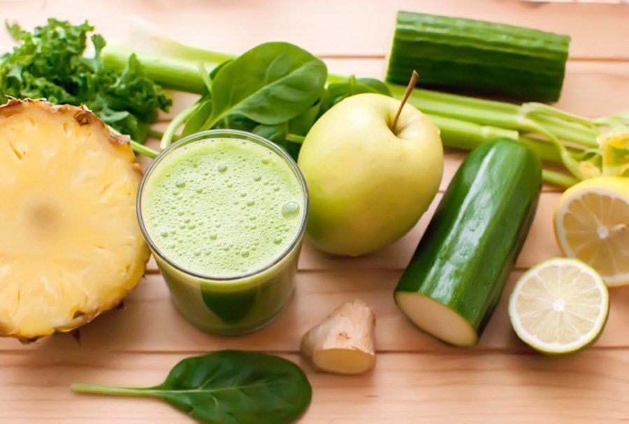 Glas grüner Saft auf Holztisch umringt von grünen und gelben Obst und Gemüse