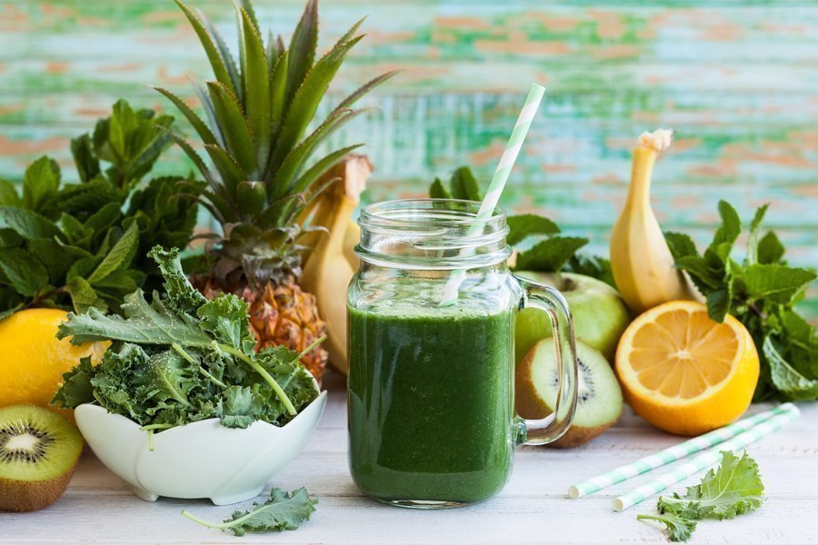 Grüner Smoothie in einem Glas mit Strohhalm und frischem Obst und Gemüse
