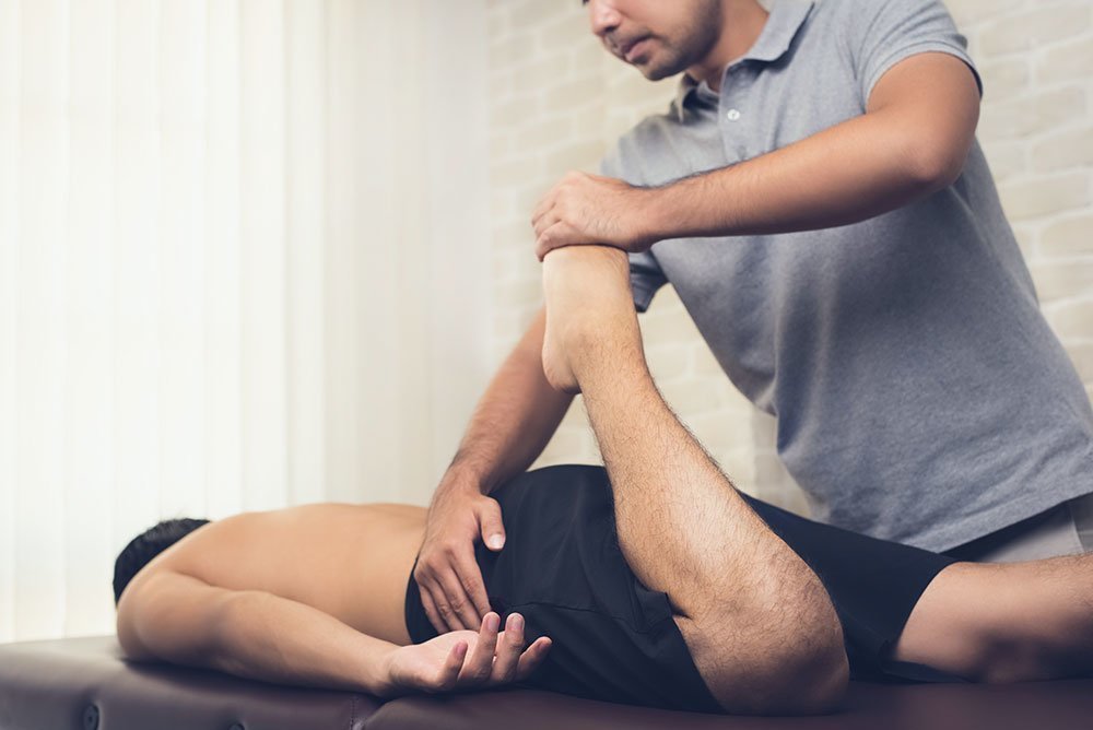 Junger Mann wird von einem Physiotherapeut mit einer Sportmassage behandelt