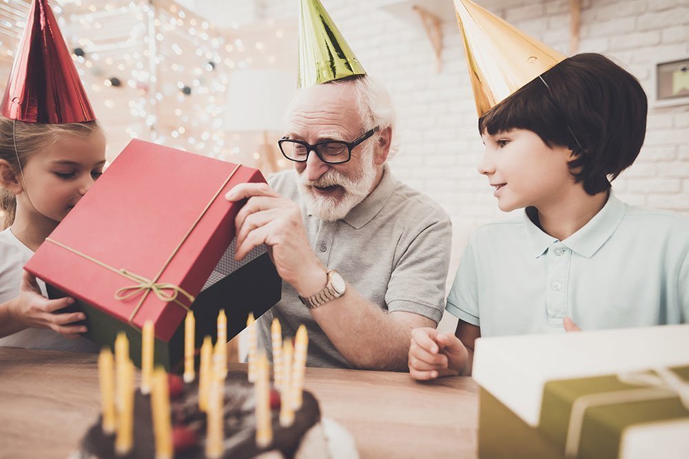Opa wird von zwei Enkeln zum Geburtstag beschenkt hinter einer Geburtstagstorte