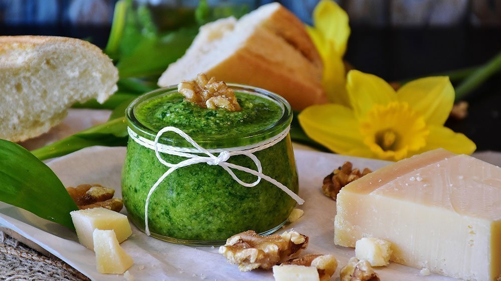 Selbstgemachtes grünes Pesto in einem Glas mit Brot, Käse und Walnüssen dekoriert